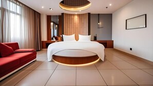 A modern hotel room with a large bed, a red sofa, a round coffee table, and a ceiling light fixture. - Jiajie Boutique Hotel (Lingao Cultural Park Fulo Plaza Branch) (Lingao)