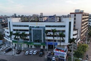 Un edificio de varios pisos con una entrada destacada, varios autos estacionados y una vista despejada del entorno urbano.