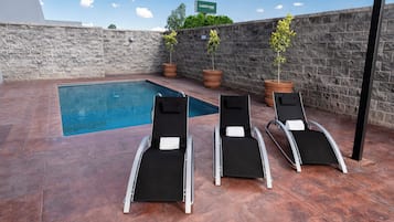 Una piscina con sillones de descanso, un muro de piedra y plantas en macetas.