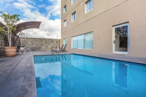 Ein Pool mit Liegestühlen, eine Steinmauer und ein Gebäude mit großen Fenstern.