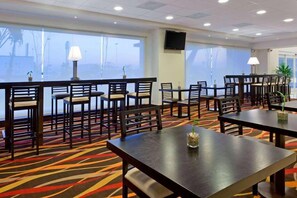 Ein Hotel-Speisesaal mit mehreren Tischen und Stühlen, einem gemusterten Teppich und großen Fenstern.