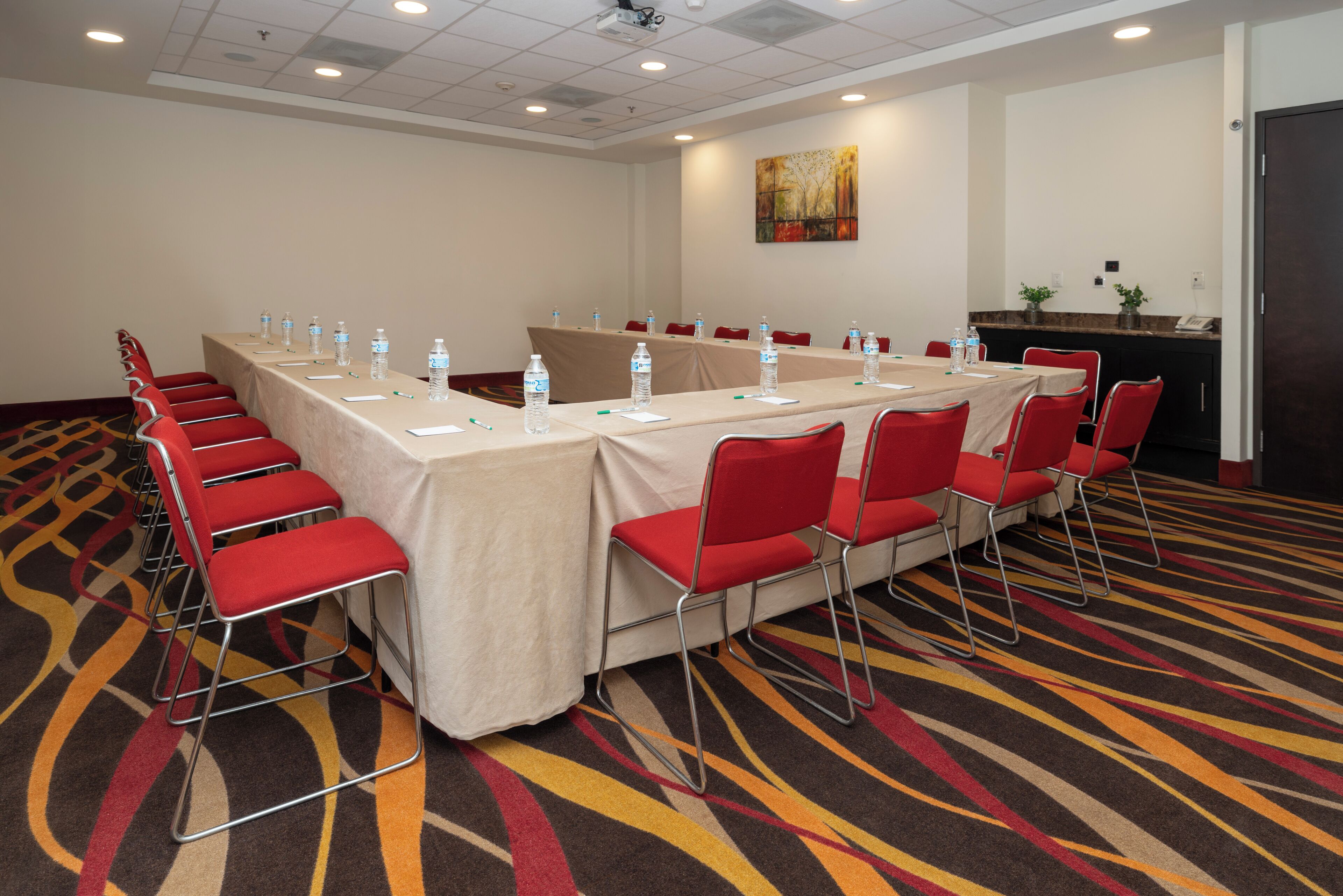 A conference room with a long table, red chairs, water bottles, and a carpeted floor.