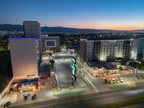 A hotel with a modern design, a parking lot, and a view of the cityscape at dusk. - Garden Park San Luis Potosí (San Luis Potosi)