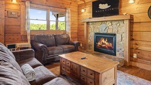 Un acogedor interior de cabaña de madera con chimenea de piedra, sofás de cuero y un televisor montado en la pared.