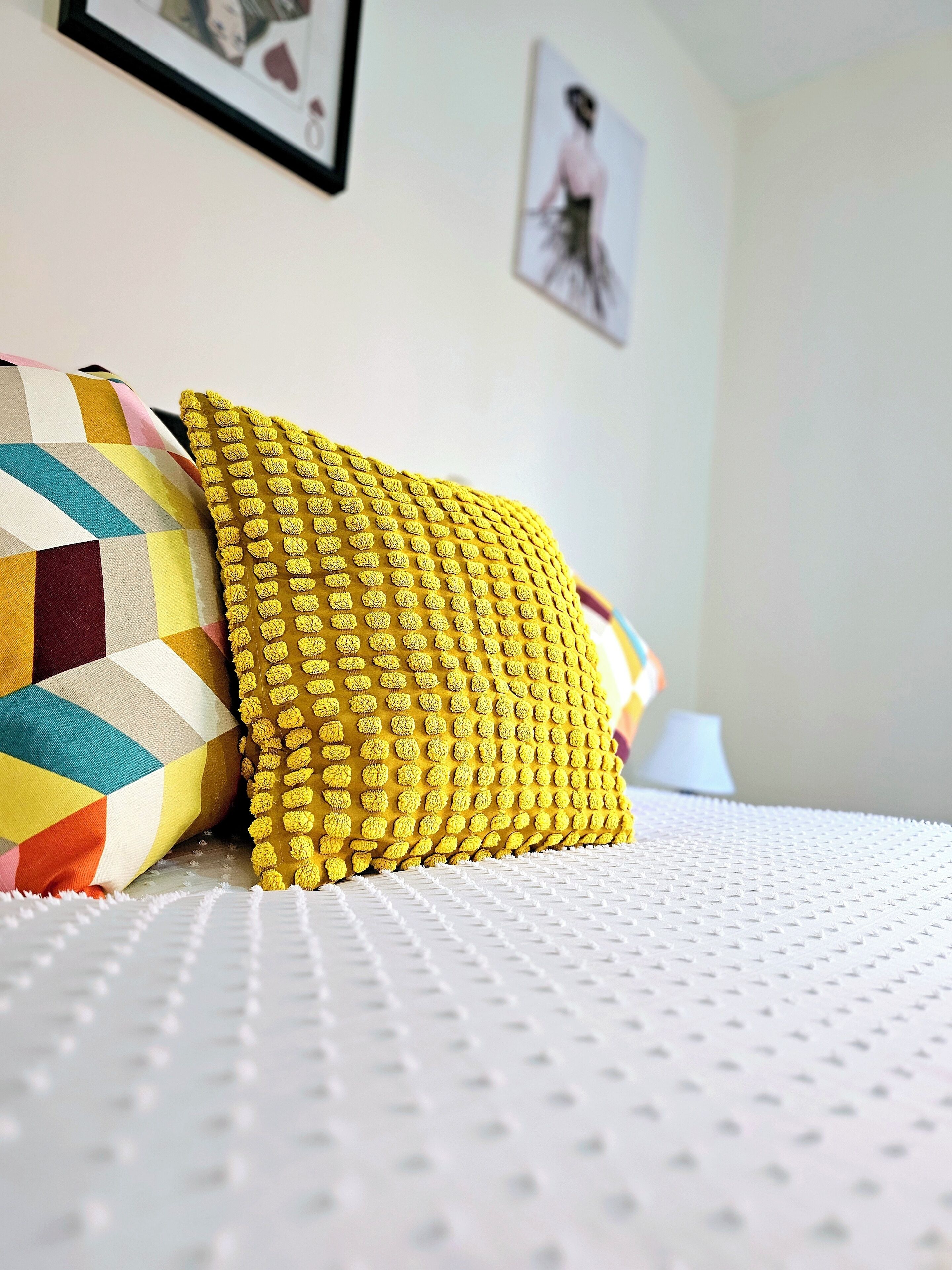 Un letto con una coperta bianca e testurizzata, un cuscino giallo testurizzato e un cuscino trapuntato multicolore.