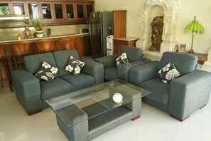 A living room with a sectional sofa, a glass coffee table, and a kitchen in the background. - Bali Emerald Villas (Bali)