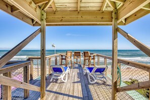 A wooden deck with two lounge chairs and a table, overlooking a beach with a clear view of the ocean. - First Floor Beachfront Condo with Patio Grill and Fire Pit (New Smyrna Beach)