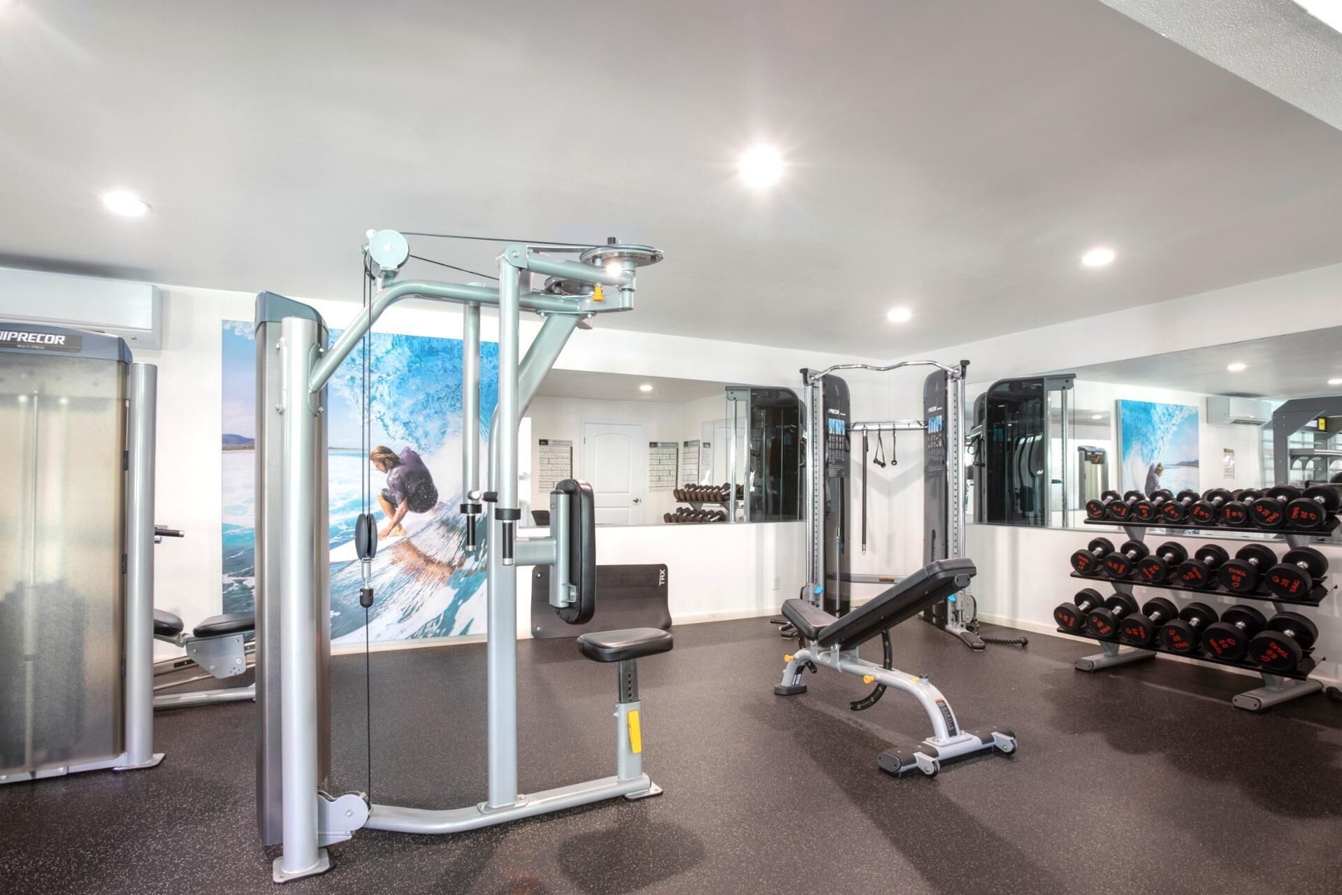 Un gimnasio con diversos equipos de ejercicio, incluyendo un banco de pesas, mancuernas y una máquina de poleas.