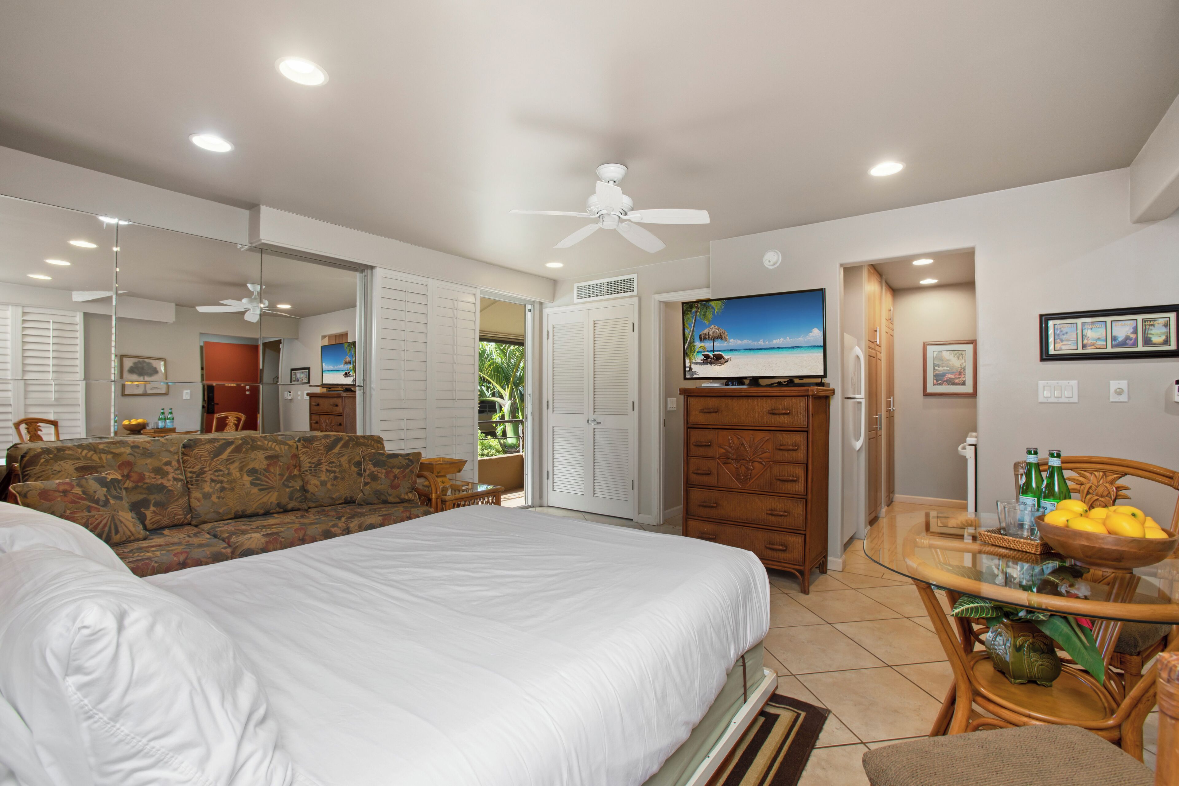 A bedroom with a large bed, a ceiling fan, a TV, and a dining area with a table and chairs.