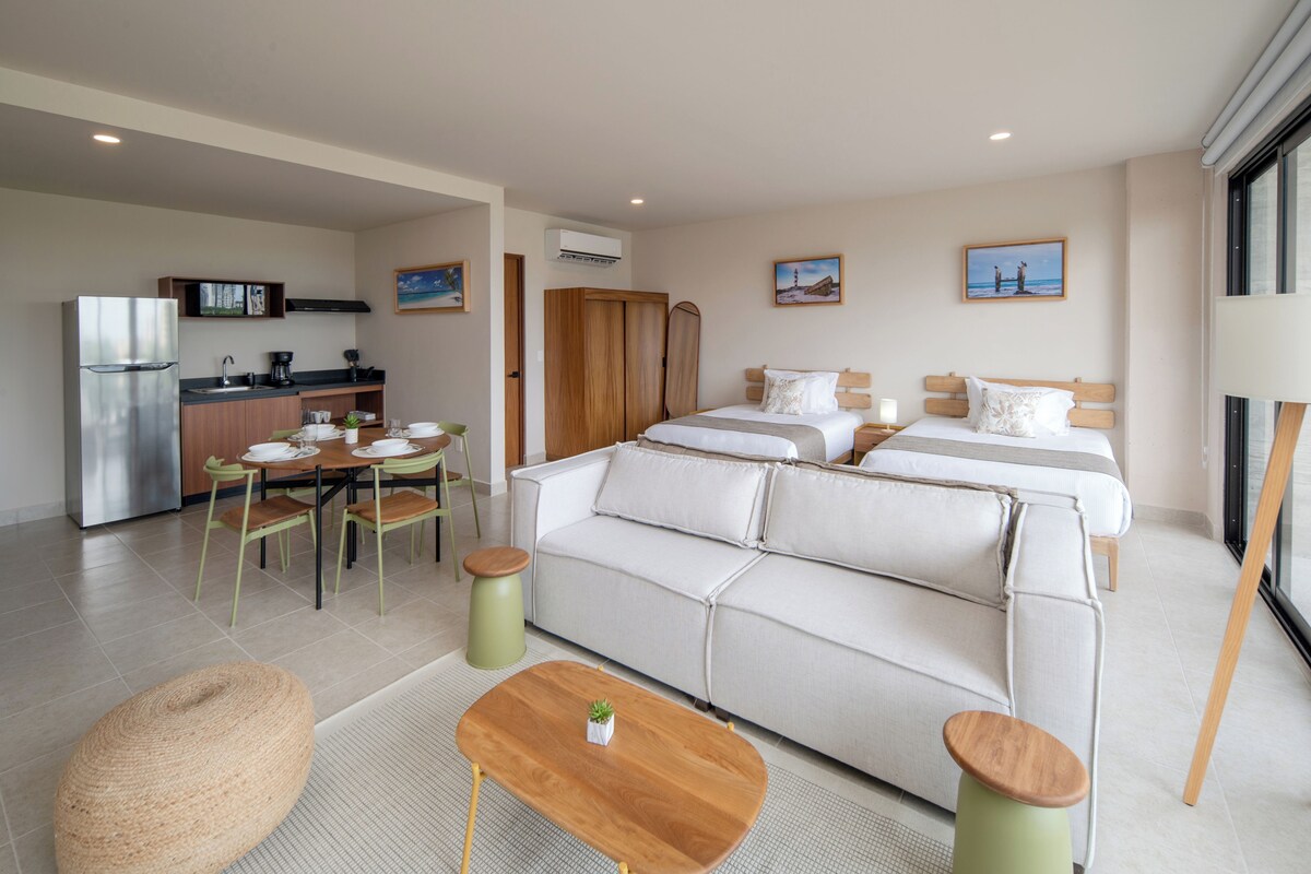 Une chambre d’hôtel moderne dotée d’une kitchenette, d’un canapé-lit, d’un coin repas et offrant une vue sur la mer.