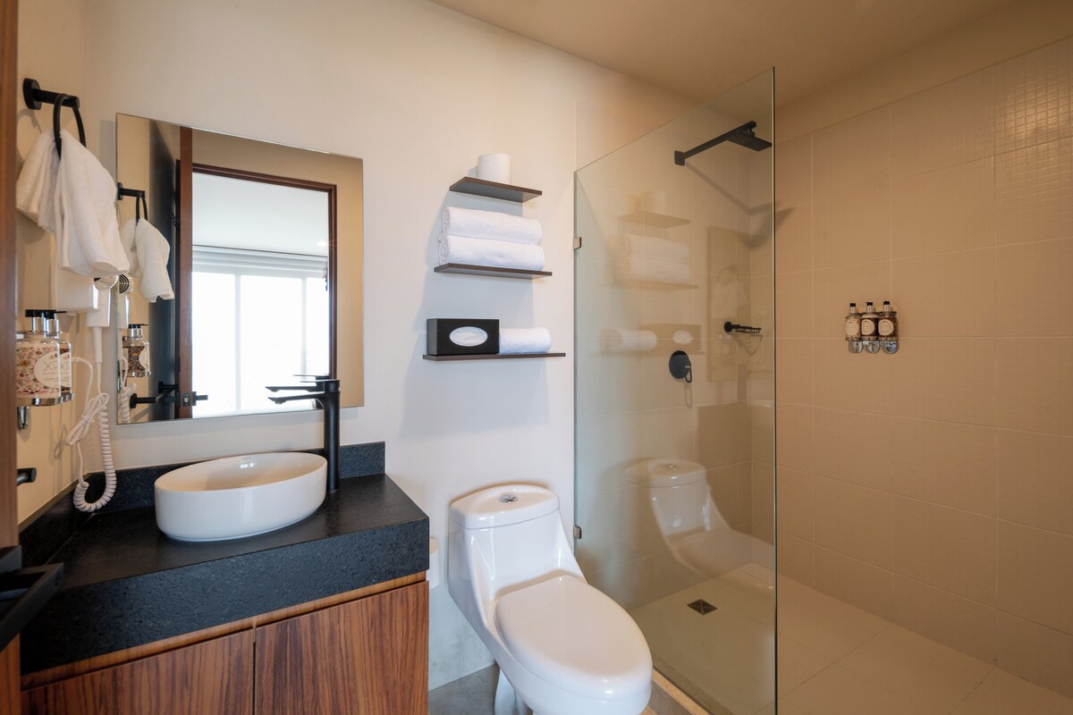 A modern bathroom with a large mirror, a sink, a toilet, and a glass-enclosed shower area.