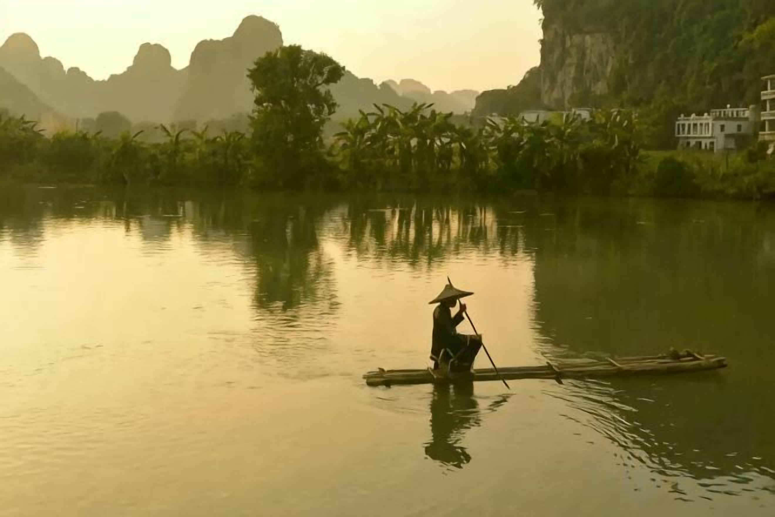 Una persona en un bote en un río tranquilo con montañas al fondo.