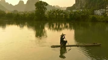 Una persona en un bote en un río tranquilo con montañas al fondo.