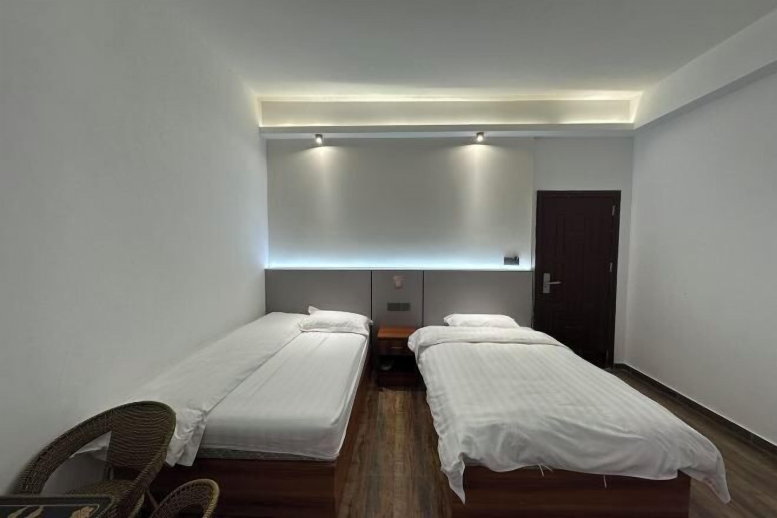 Une petite chambre propre, avec deux lits simples, un plancher en bois et une porte sombre.