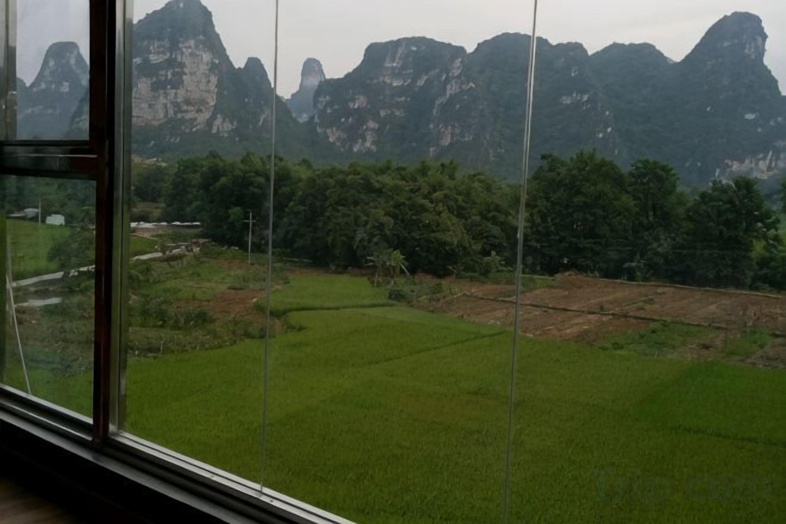 A view through a window with a landscape of green fields and distant mountains.