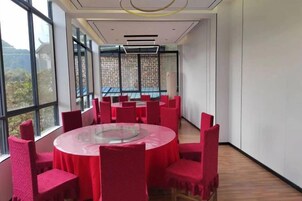 Un salón de conferencias con una mesa redonda rodeada de sillas rojas, ventanas amplias y vista a un edificio.