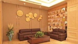 A modern living room with two brown sofas, a coffee table with a plant, and a bookshelf filled with books and decorative items. - GreenTree (Shuyang Development Zone Yingbin Avenue) (Shuyang)