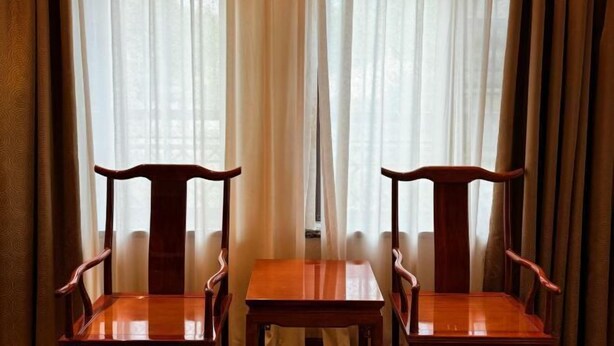 Dos sillas de madera y una mesita frente a una ventana con cortinas traslúcidas.
