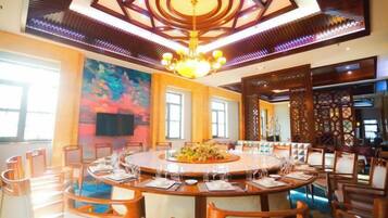 A spacious dining area with a round table surrounded by chairs, a chandelier, and a large painting on the wall.