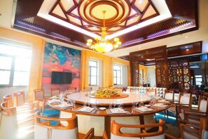 A spacious dining area with a round table surrounded by chairs, a chandelier, and a large painting on the wall.