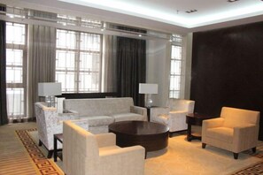A hotel room with a sofa set, two armchairs, a coffee table, and a large window with curtains.