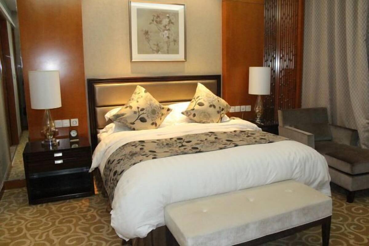A hotel room with a bed, bedside tables, a chair, and a wall-mounted artwork.