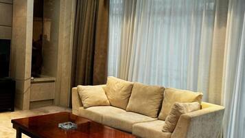 A living room with a beige sofa, a wooden coffee table, and a large window with sheer curtains.