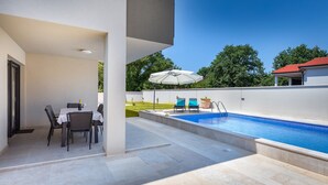 Zona de piscina al aire libre con una mesa y sillas, un espacio de estar cubierto con una sombrilla y vistas del paisaje circundante.