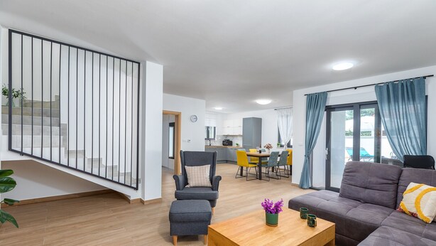 Una sala moderna con un sofá, una mesa de centro y una silla. Se ve una escalera con barandilla que conduce a un piso superior.
