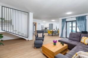 Una sala moderna con un sofá, una mesa de centro y una silla. Se ve una escalera con barandilla que conduce a un piso superior.