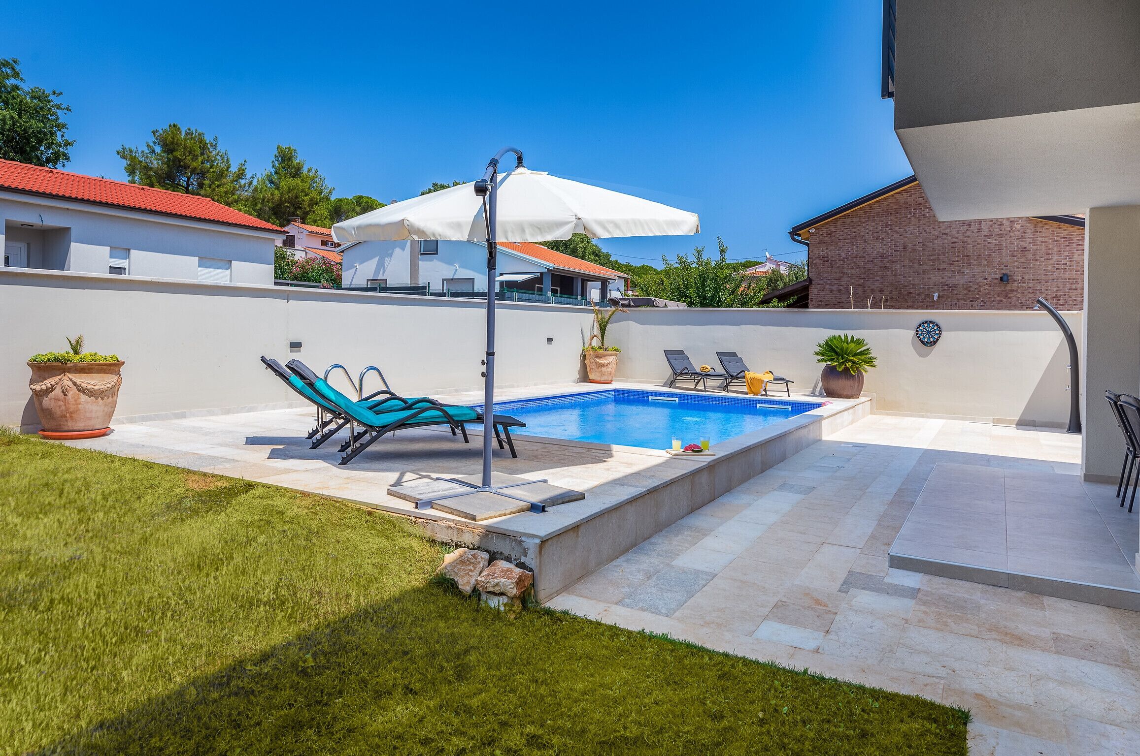 A swimming pool with lounge chairs and an umbrella, surrounded by a well-maintained lawn and a brick wall.