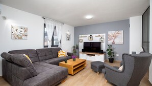 Una sala moderna con un sofá gris, una mesa de centro de madera, un sillón gris y un televisor de pantalla plana sobre un mueble blanco.