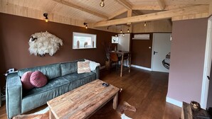 A cozy living room with a wooden ceiling, a green sofa with pink cushions, a wooden coffee table, and a rustic sheep decoration.