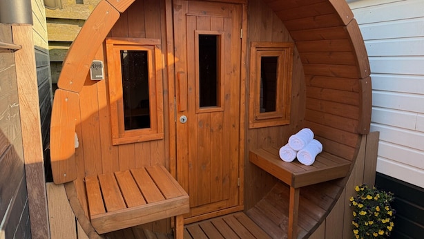 A wooden sauna with two windows, a bench, and a small shelf with towels.