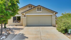 A single-story house with a garage, a sloped roof, and a front yard with a tree and shrubs. - Tucson Home w/ Patio, Grill & Mountain Views! (Tucson)