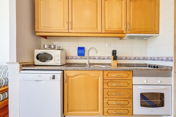 A compact kitchen with wooden cabinets, a microwave, a dishwasher, a sink, and a stove.