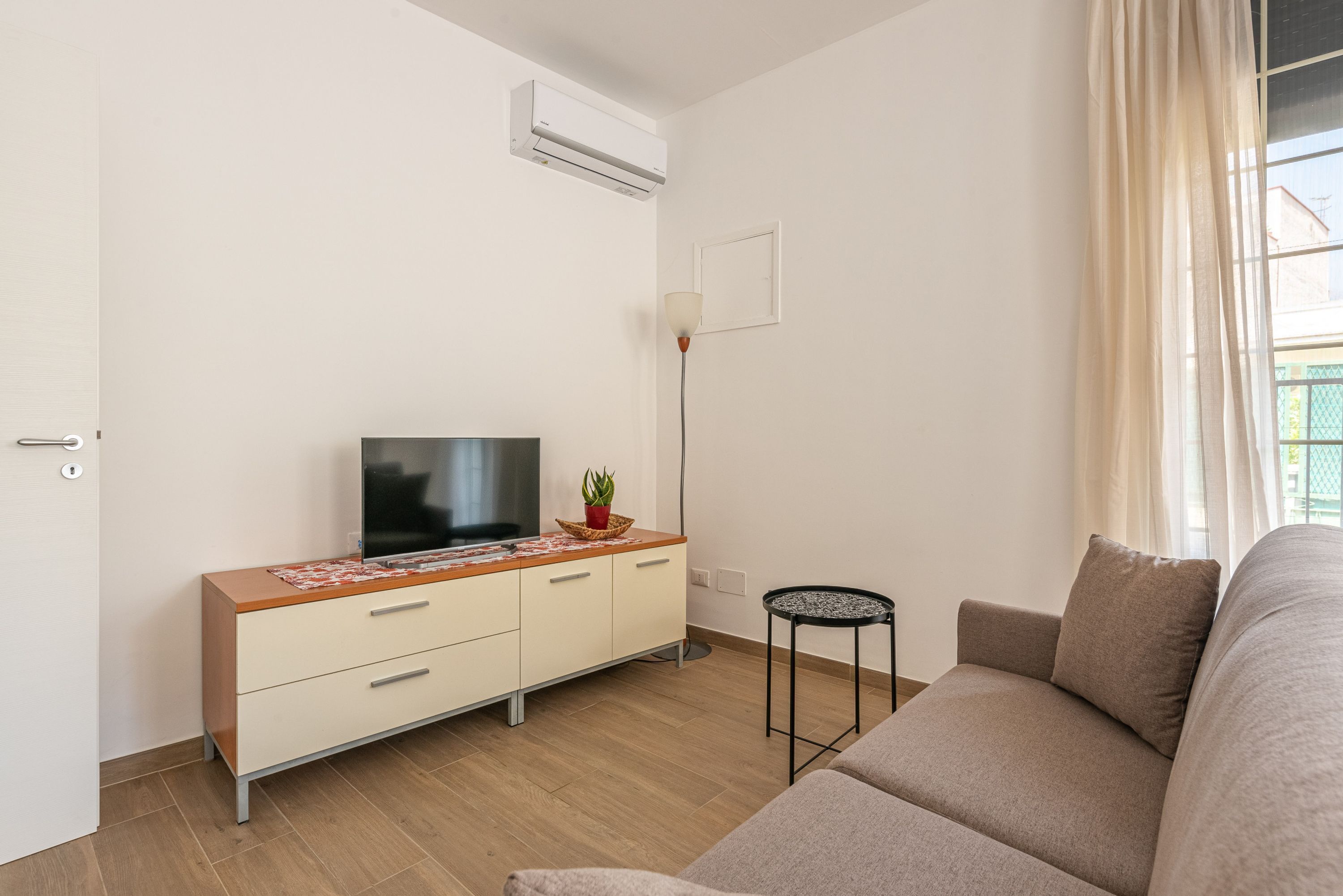 Una sala moderna con un televisor de pantalla plana sobre un mueble de madera, una mesita redonda y un sofá.