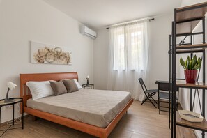 A hotel room with a wooden bed, a small table with a lamp, a chair, a potted plant, and a wall-mounted shelf. - La Casa Donna Vita a Mondello by Wonderful Italy (Palermo)