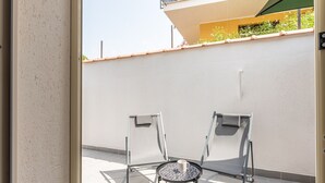 Un balcon avec deux chaises et une petite table ronde, un mur blanc et un sol carrelé.