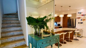 A modern kitchen with a bar area, a staircase, and a large plant on a teal console table. - Cozy 3 Bedroom Penthouse in Playa Bonita (Las Terrenas)