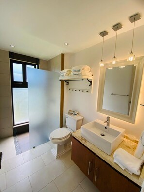 A modern bathroom with a toilet, sink, and mirror. There is a towel rack above the sink and a window providing natural light.