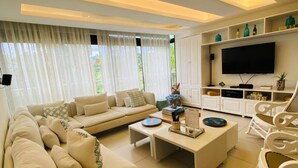 A modern living room with a sofa set, a coffee table, and a TV on a white cabinet. - Cozy 3 Bedroom Penthouse in Playa Bonita (Las Terrenas)