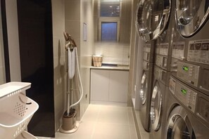 A laundry room with stacked washing machines and dryers, a drying rack, and a washing machine with a hose. - Homeinn · neo (Shijiazhuang Xinbai Square Wanli Temple Pedestrian Street) (Shijiazhuang)