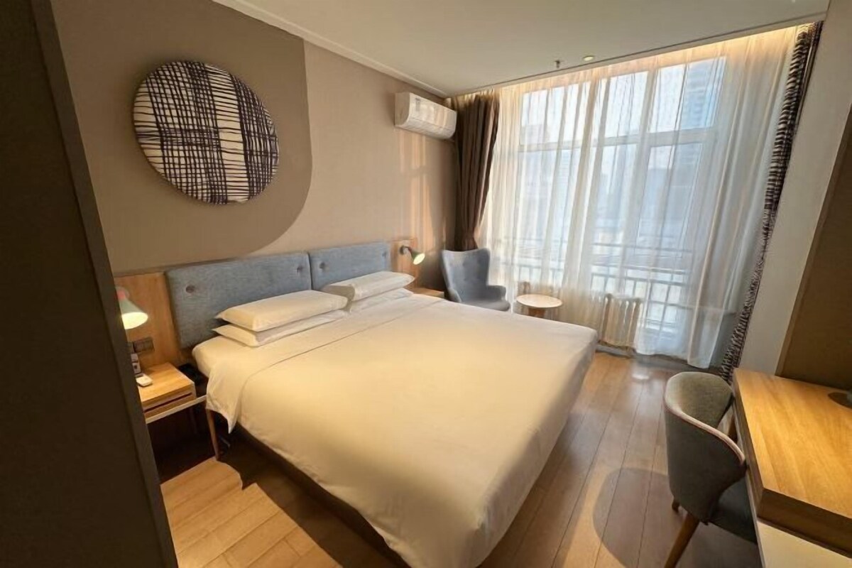Ein Hotelzimmer mit einem großen Bett, einem Schreibtisch, einem Stuhl, einer runden Wanddekoration und einem Fenster mit Vorhängen.