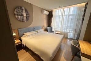 Ein Hotelzimmer mit einem großen Bett, einem Schreibtisch, einem Stuhl, einer runden Wanddekoration und einem Fenster mit Vorhängen.