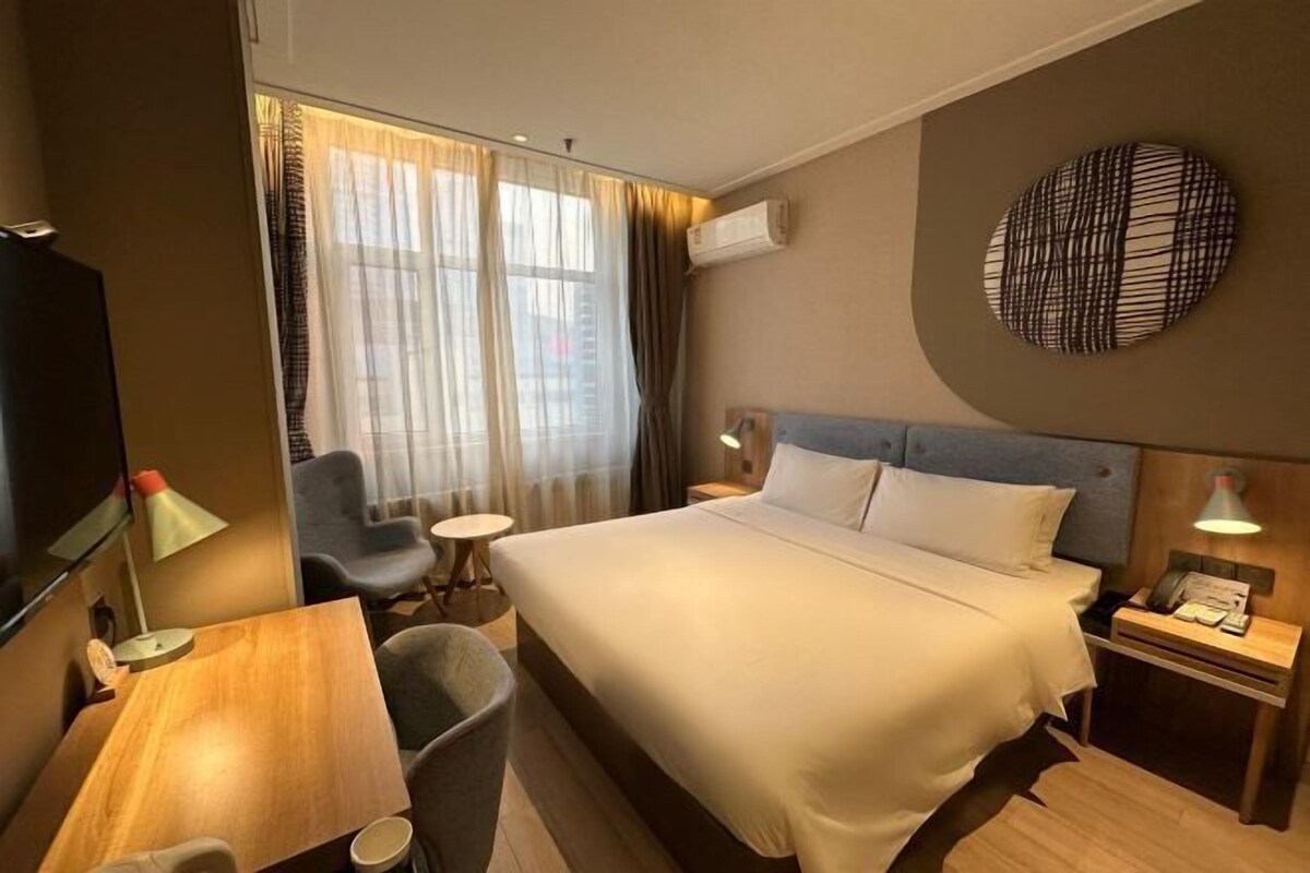 Ein Hotelzimmer mit einem Bett, einem Schreibtisch, einem Sessel, einem kleinen Tisch und einem Fernseher.