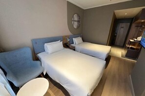 Ein Hotelzimmer mit zwei Betten, einem Schreibtisch, einem Sessel und einem Fernseher.