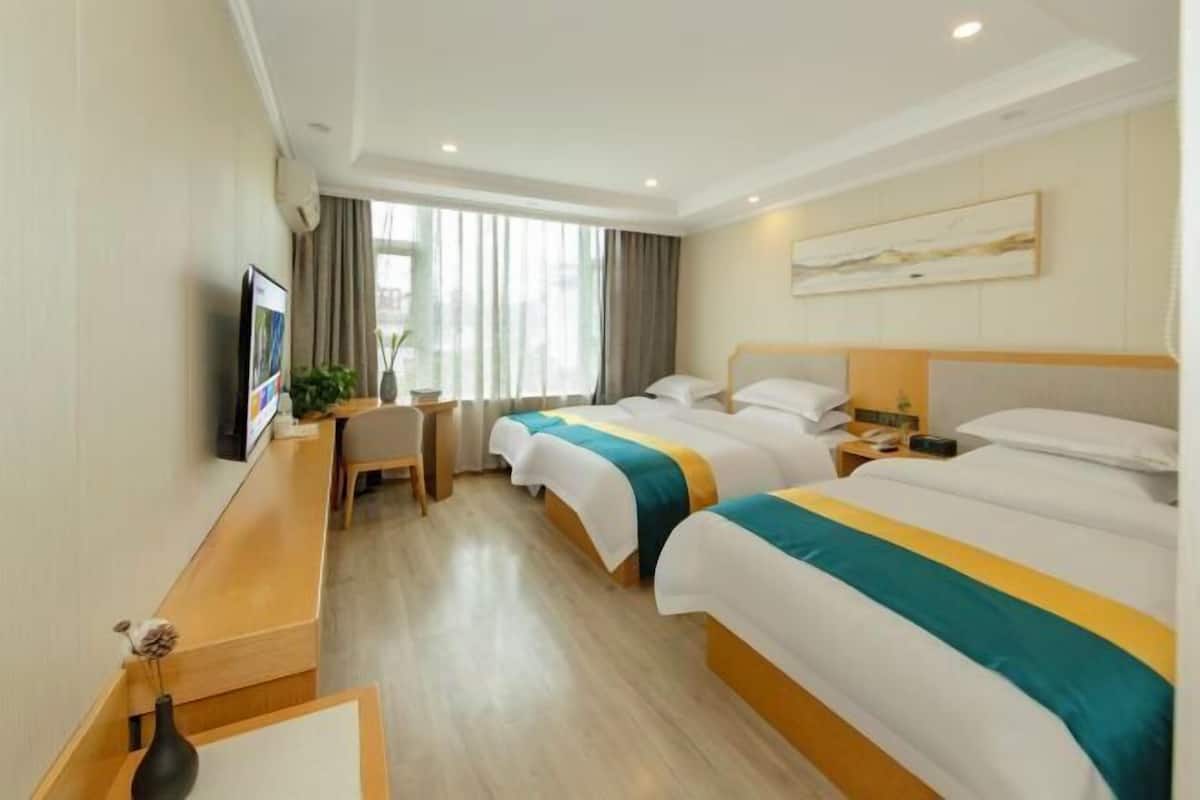 Ein Hotelzimmer mit zwei Betten, einem Schreibtisch, einem Stuhl, einem Fernseher und einem Fenster mit Vorhängen.