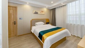 A hotel room with a bed, a wooden door, a painting on the wall, and a window with curtains. - Boffin Holiday Inn (Lijiang)