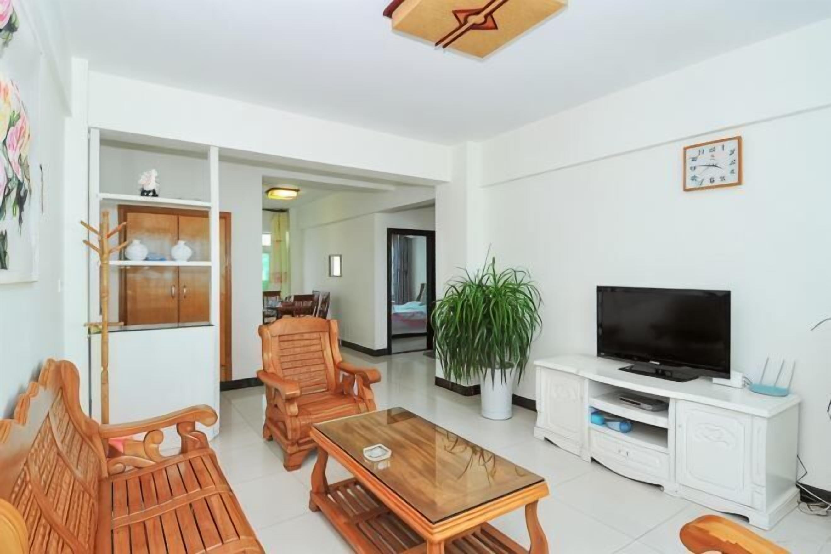 Un salon avec un téléviseur, des meubles en bois, une plante et un meuble blanc.